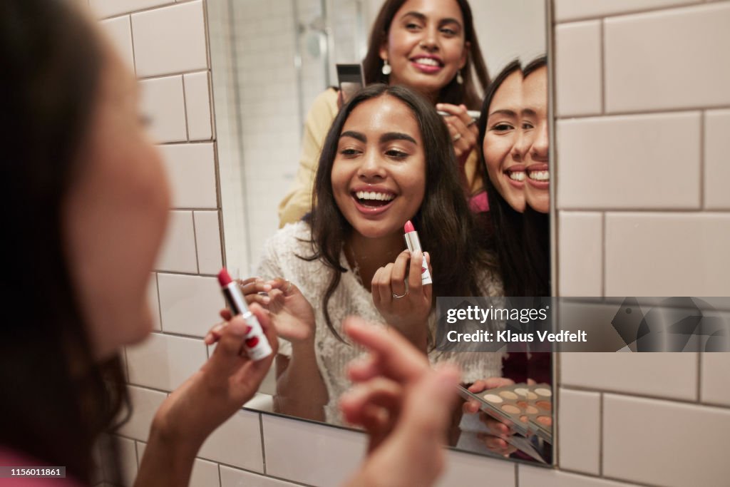 Smiling friends with lipstick looking at mirror