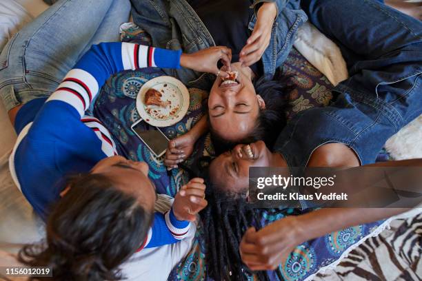 woman feeding bread to smiling friend on bed - slumber party - fotografias e filmes do acervo