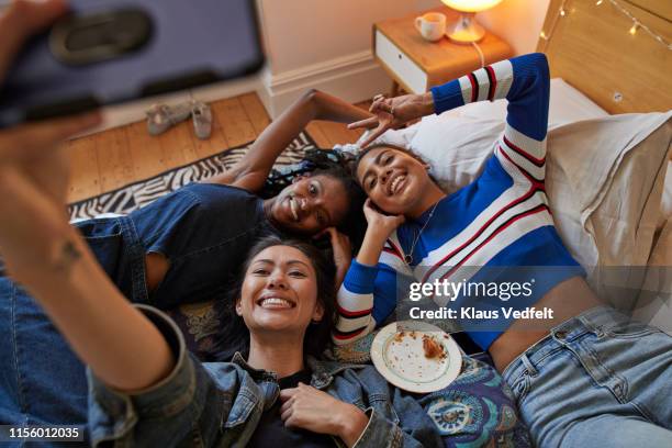 woman taking selfie with happy friends on bed - roommate stock-fotos und bilder