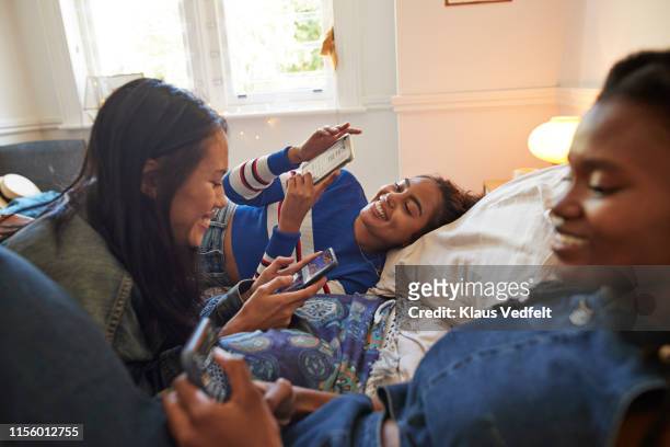 Smiling young female friends using phones at home