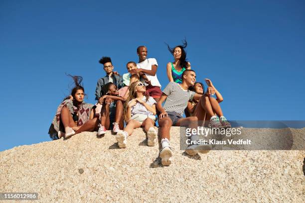 multi-ethnic friends sitting together on rock - reisegruppe stock-fotos und bilder