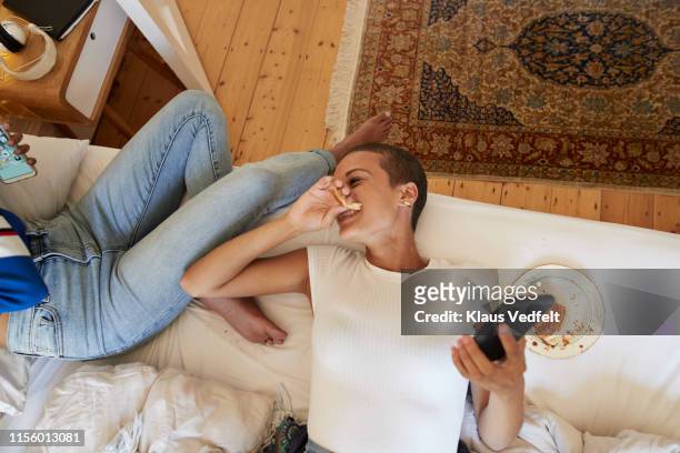 cheerful woman looking at friend sitting on bed - young woman eating stockfoto's en -beelden
