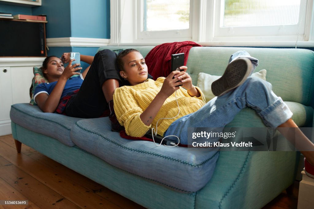 Friends using mobile phones while lying on sofa