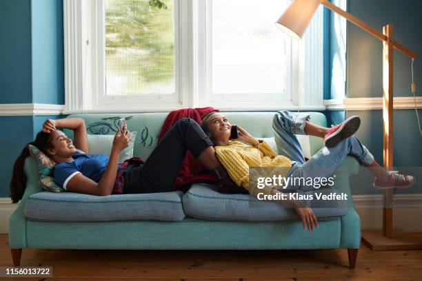 smiling friends using phone while lying on sofa - lamp foto e immagini stock