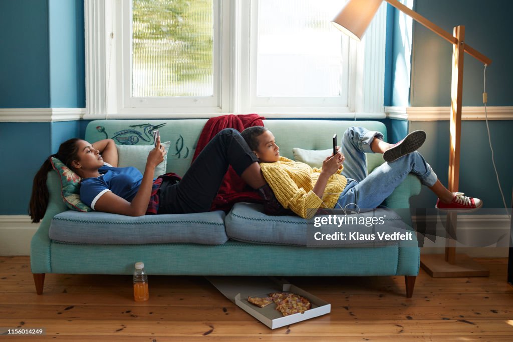 Women using phones while relaxing on sofa