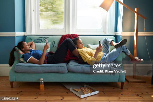 women using phones while relaxing on sofa - roommate bildbanksfoton och bilder