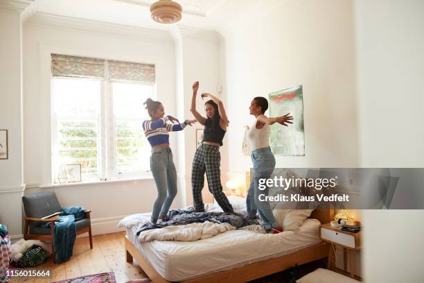 cheerful young women dancing on bed at home - weekend activiteiten stockfoto's en -beelden