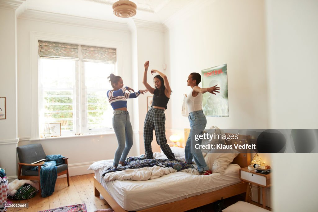 Cheerful young women dancing on bed at home
