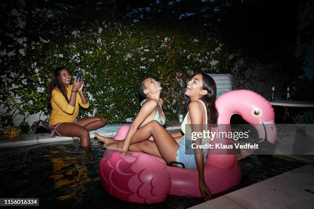 woman photographing friends relaxing on pink raft - pool party night stock pictures, royalty-free photos & images