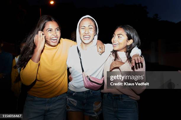 cheerful female friends with arm around at night - yellow coat stock-fotos und bilder