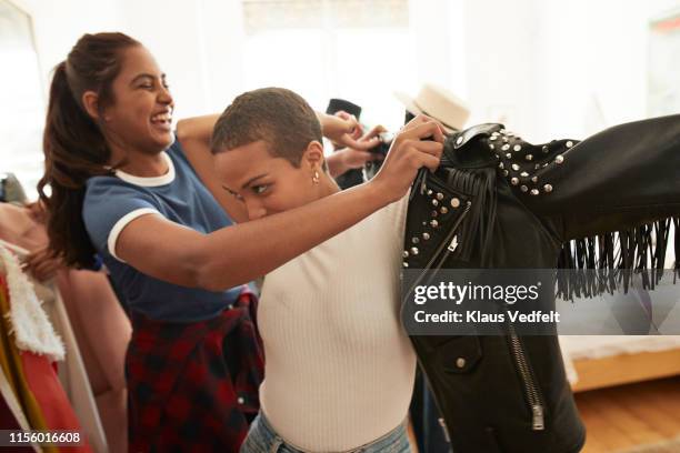 woman helping friend wearing black leather jacket - getting dressed stockfoto's en -beelden