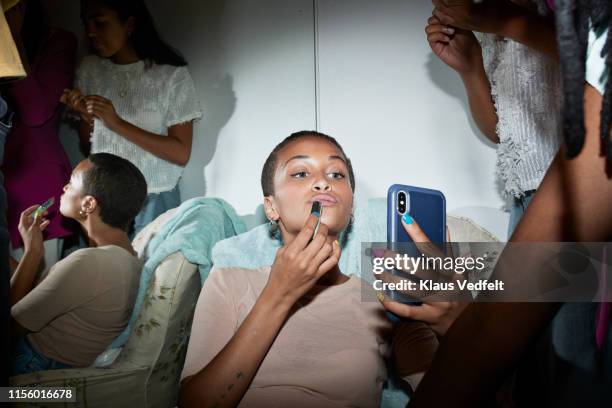 female applying lipstick while looking in mobile phone - black mirror imagens e fotografias de stock