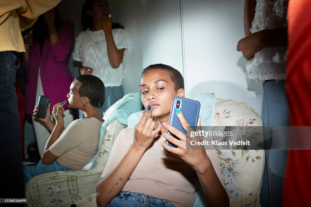 Woman applying lipstick while looking in smart phone