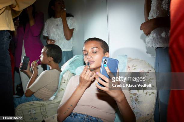 woman applying lipstick while looking in smart phone - 浮華 個照片及圖片檔