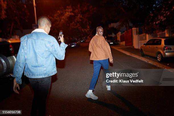 man photographing friend on smart phone at street - fashion photography stockfoto's en -beelden