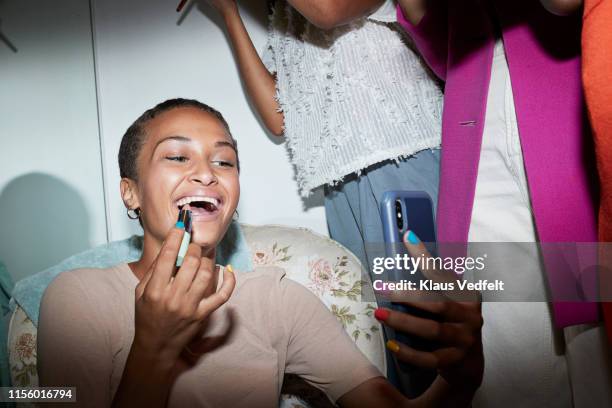 cheerful woman with smart phone applying lipstick - making stock-fotos und bilder