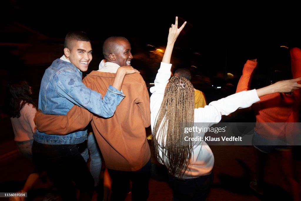Cheerful males dancing with friends at night