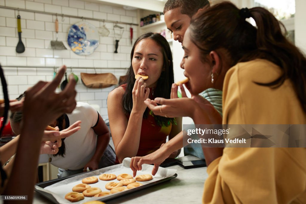 Friends eating fresh cookies in kitchen at home