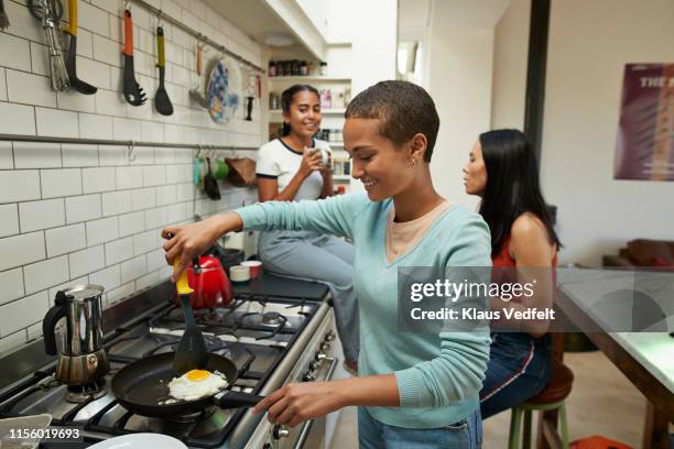 smiling woman preparing fried egg in kitchen - flatmate stock pictures, royalty-free photos & images