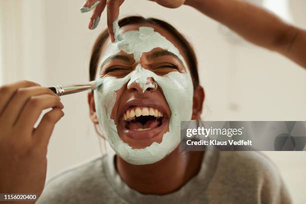 hands of friends spreading cream on woman's face - applying makeup with brush foto e immagini stock