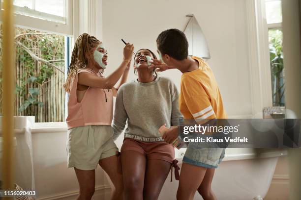 cheerful friends enjoying while applying cream - applying makeup with brush fotografías e imágenes de stock