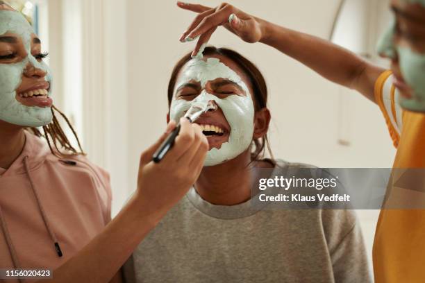 young woman enjoying friend's applying cream on face - applying makeup with brush foto e immagini stock