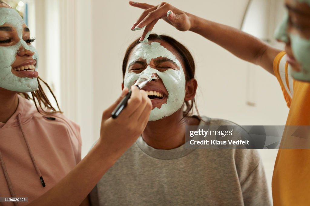 Young woman enjoying friend's applying cream on face