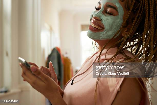 cheerful woman using smart phone at home - mask joke stockfoto's en -beelden