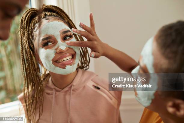 woman applying cream on friend's face with finger - gesicht kosmetik maske stock-fotos und bilder