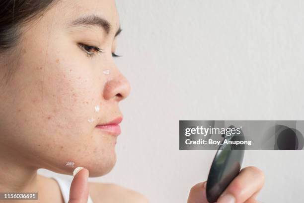 portrait of young asian woman applying acne cream/moisturizer on her face by looking a pocket mirror. - applying cream stock pictures, royalty-free photos & images