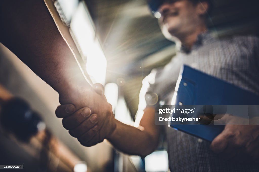 Fermez-vous vers le haut de l'inspecteur serrant la main avec la personne méconnaissable dans une usine.