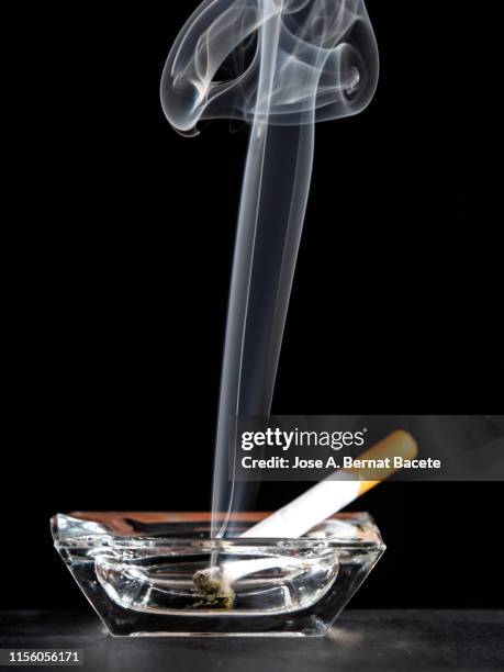 lighted cigarette with smoke trail inside an ashtray on a black background. - ashtray stock pictures, royalty-free photos & images