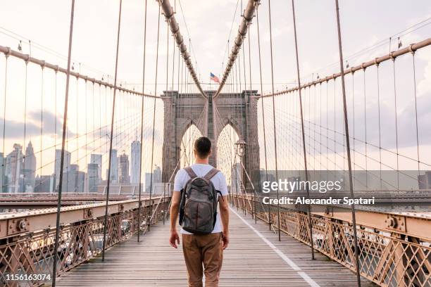 rear view of a young man with backpack walking on brooklyn bridge, new york city, usa - journey fotografías e imágenes de stock