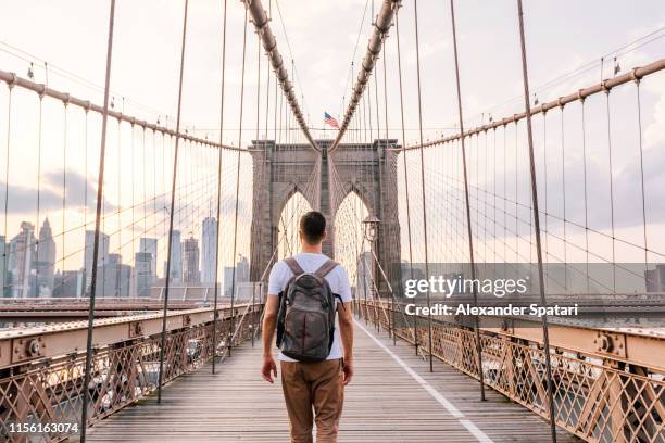 rear view of a young man with backpack walking on brooklyn bridge, new york city, usa - ponte de brooklyn imagens e fotografias de stock