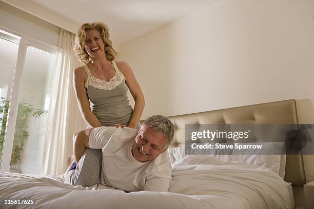 mature couple wrestling on bed - woman straddling man stock pictures, royalty-free photos & images