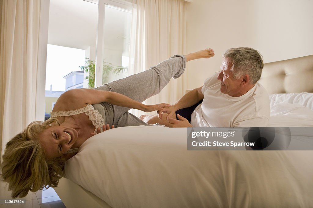 Mature couple wrestling on bed