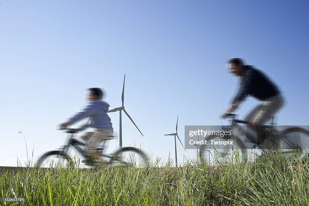 Father and son cycling past a windfarm