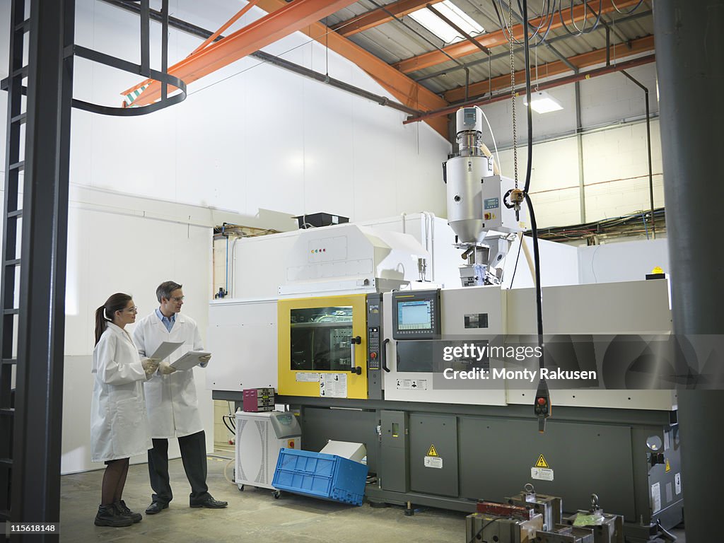 Male and female scientists next to plastic moulding machine holding notes