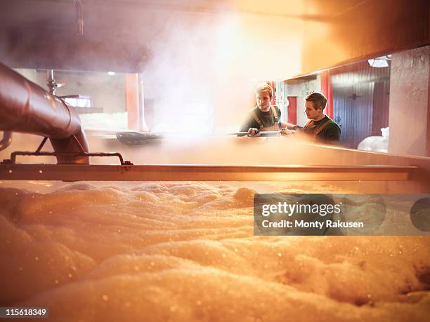 workers with tank of hot wort in brewery - brauerei stock-fotos und bilder