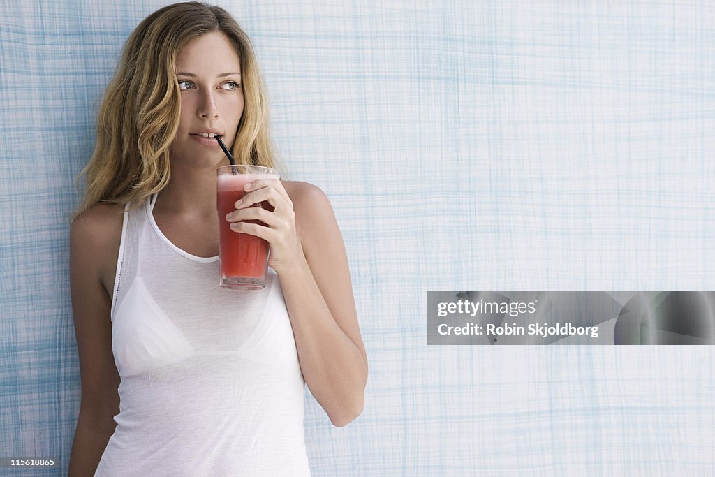 Girl up against blue wall with red smoothie, looking to the side