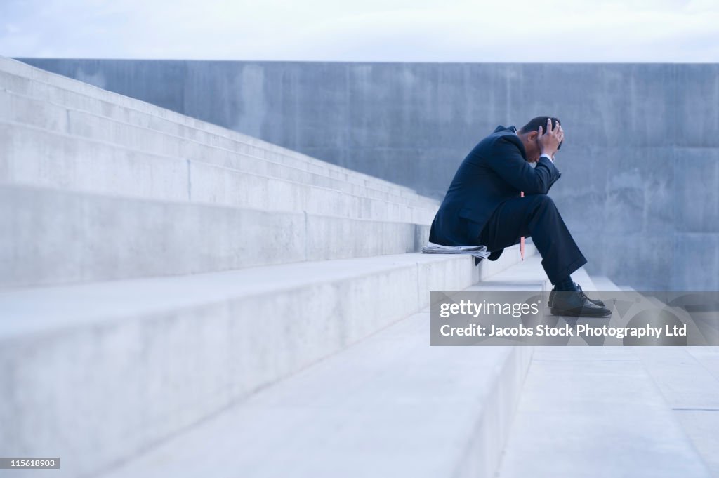 Frustrated Hispanic businessman sitting on steps