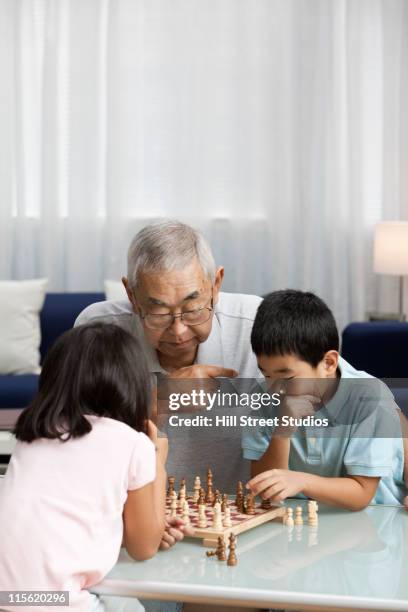 asian grandfather and grandchildren playing chess - multi generation family thinking stock pictures, royalty-free photos & images