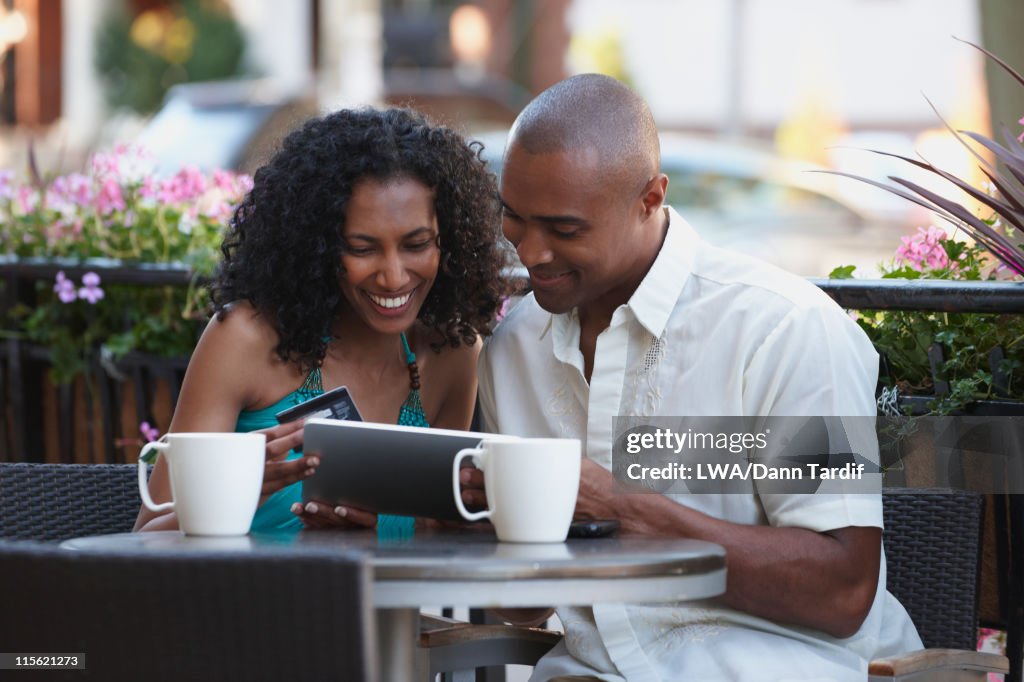 Couple with credit card in cafe looking at digital tablet together
