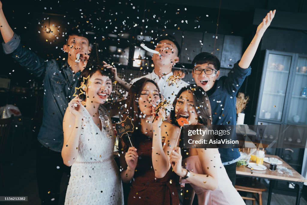 Groep van vrolijke jonge Aziatische man en vrouw Holding rekwisieten en vieren met confetti tijdens de partij