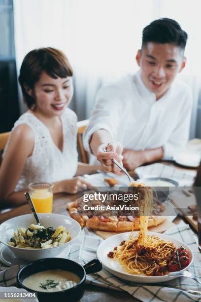 young asian man serving pasta to friends during party, they are having fun, chatting and enjoying food and drinks - the joys of eating spaghetti stock pictures, royalty-free photos & images