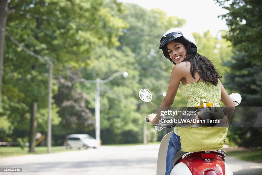 Hispanic teenager riding scooter with groceries