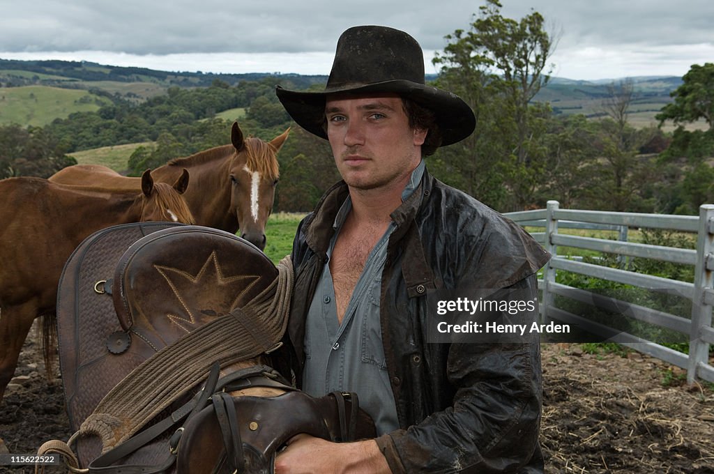 Horse rider holding saddle with horses