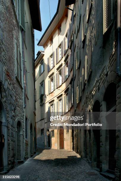 Italy; Lombardy; Bergamo; Citta Alta. View Bergamo street alley buildings windows shutters rusticated arches stone walls doorways