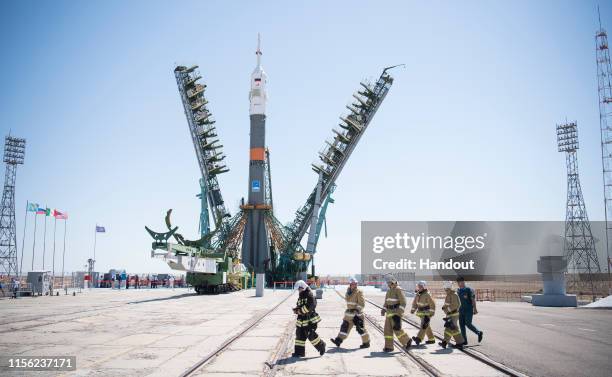 In this handout image provided by NASA, Firefighters walk past the Soyuz rocket as the service structure arms are closed around it, at Baikonur...