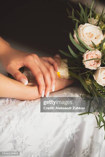 the bride in an elegant openwork wedding dress is holding a beautiful wedding bouquet of white or beige roses and green leaves. hands girls with gentle neat manicure close-up. wedding theme - yellow retro dress stock pictures, royalty-free photos & images